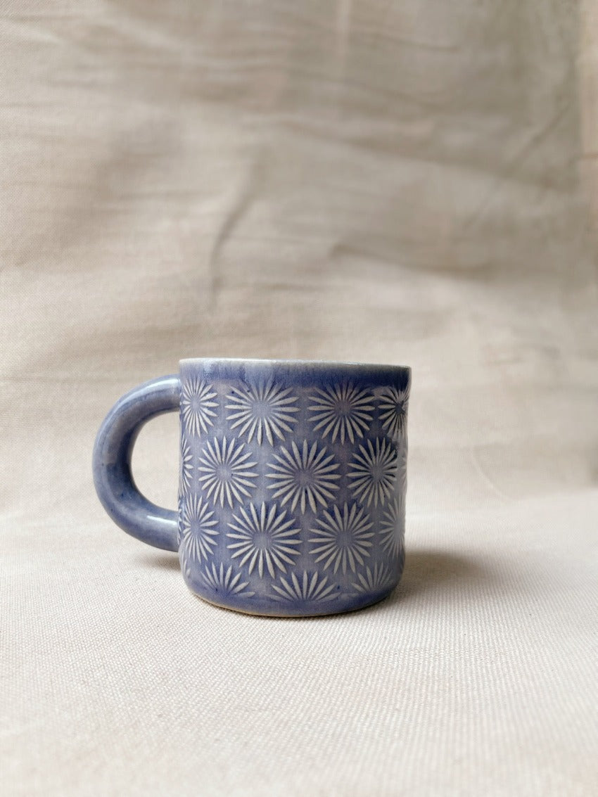 taza de cerámica hecha a mano con esmalte morado brillante y relieve de margaritas.