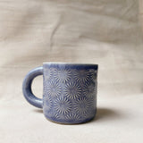 taza de cerámica hecha a mano con esmalte morado brillante y relieve de margaritas.