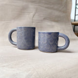 taza de cerámica hecha a mano con esmalte morado brillante y relieve de margaritas.