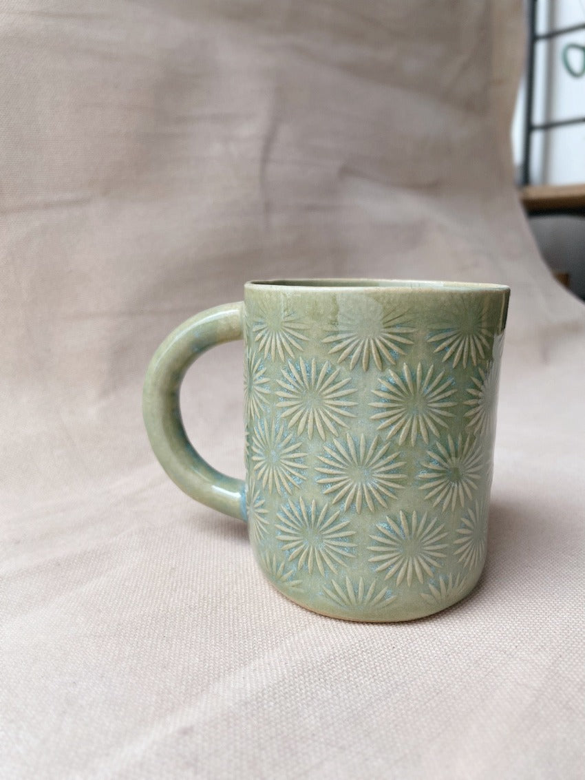 taza de cerámica hecha a mano con esmalte verde brillante y chipas celestes y relieve de margaritas.