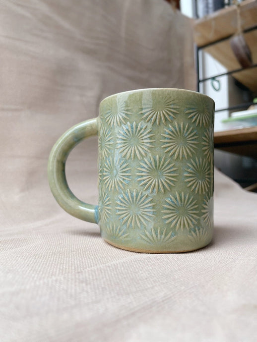 taza de cerámica hecha a mano con esmalte verde brillante y chipas celestes y relieve de margaritas.
