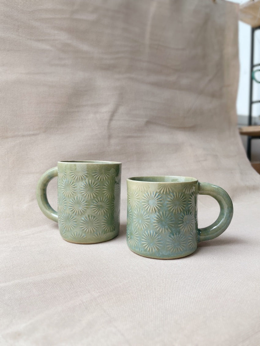 taza de cerámica hecha a mano con esmalte verde brillante y chipas celestes y relieve de margaritas.