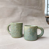 taza de cerámica hecha a mano con esmalte verde brillante y chipas celestes y relieve de margaritas.