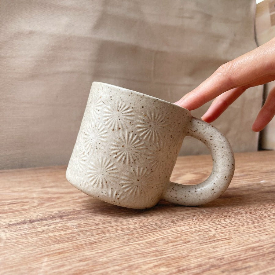taza de cerámica hecha a mano con esmalte biege neutro y relieve de margaritas.