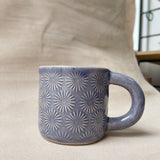 taza de cerámica hecha a mano con esmalte morado brillante y relieve de margaritas.