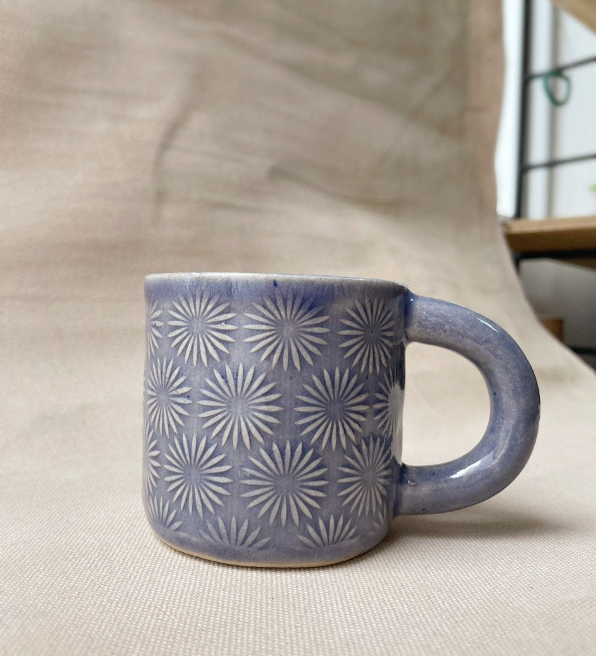 taza de cerámica hecha a mano con esmalte morado brillante y relieve de margaritas.
