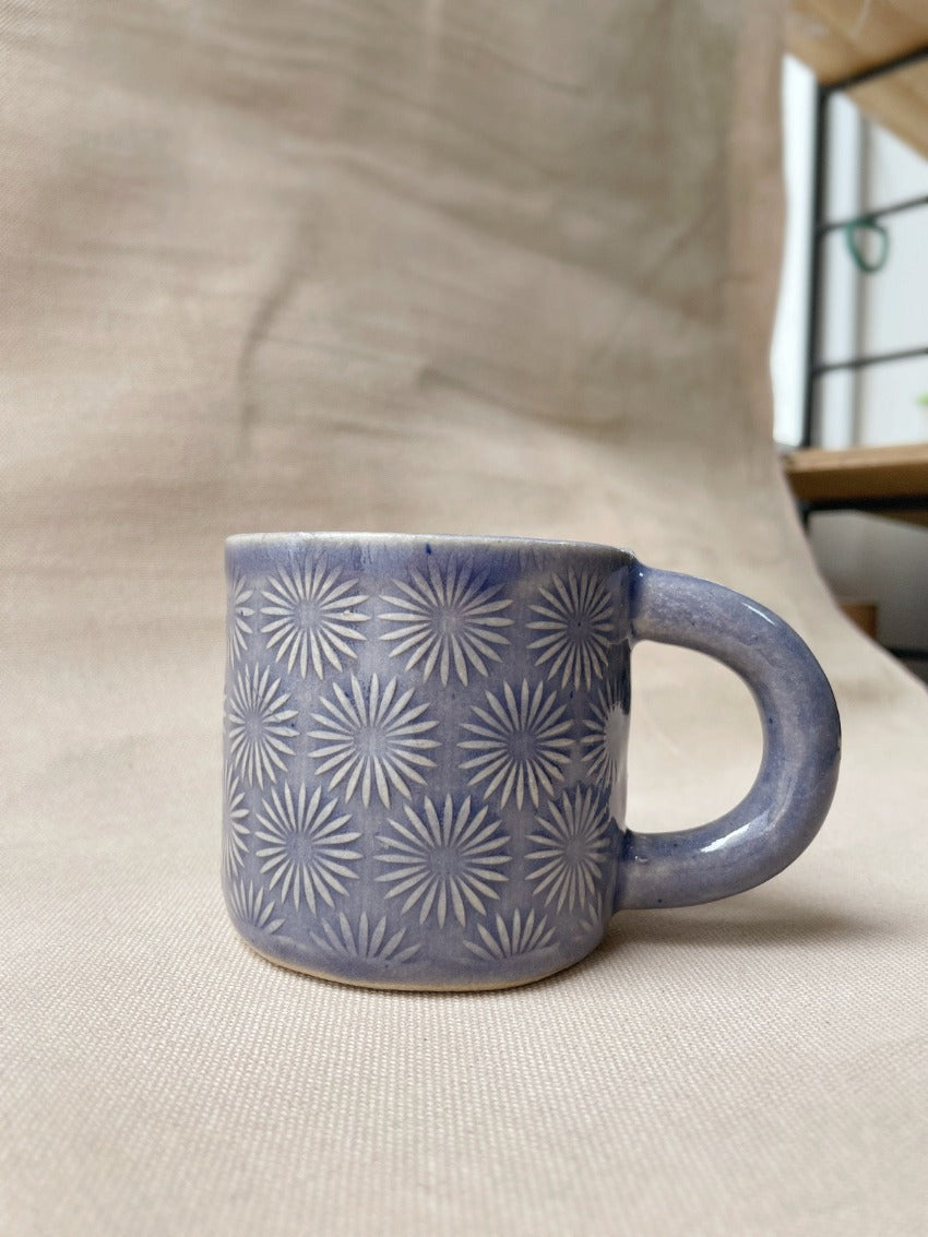 taza de cerámica hecha a mano con esmalte morado brillante y relieve de margaritas.