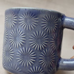 taza de cerámica hecha a mano con esmalte morado brillante y relieve de margaritas.