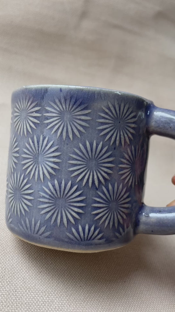 taza de cerámica hecha a mano con esmalte morado brillante y relieve de margaritas.