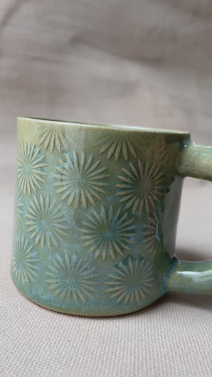 taza de cerámica hecha a mano con esmalte verde brillante y chipas turquesas y relieve de margaritas.