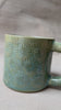 taza de cerámica hecha a mano con esmalte verde brillante y chipas turquesas y relieve de margaritas.