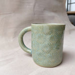 taza de cerámica hecha a mano con esmalte verde brillante y chipas celestes y relieve de margaritas.