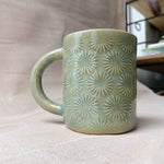 taza de cerámica hecha a mano con esmalte verde brillante y chipas celestes y relieve de margaritas.