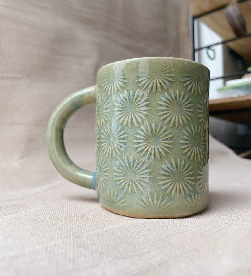 taza de cerámica hecha a mano con esmalte verde brillante y chipas celestes y relieve de margaritas.