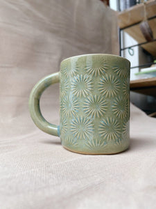 taza de cerámica hecha a mano con esmalte verde brillante y chipas celestes y relieve de margaritas.