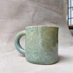 taza de cerámica hecha a mano con esmalte verde brillante y chipas turquesas y relieve de margaritas.