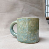 taza de cerámica hecha a mano con esmalte verde brillante y chipas turquesas y relieve de margaritas.