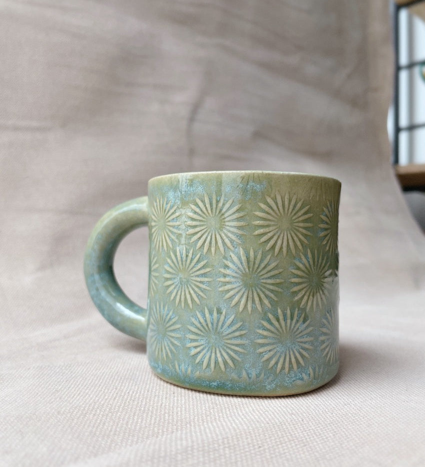 taza de cerámica hecha a mano con esmalte verde brillante y chipas turquesas y relieve de margaritas.
