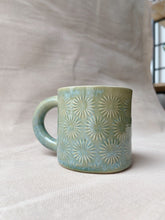 Cargar imagen en el visor de la galería, taza de cerámica hecha a mano con esmalte verde brillante y chipas turquesas y relieve de margaritas.
