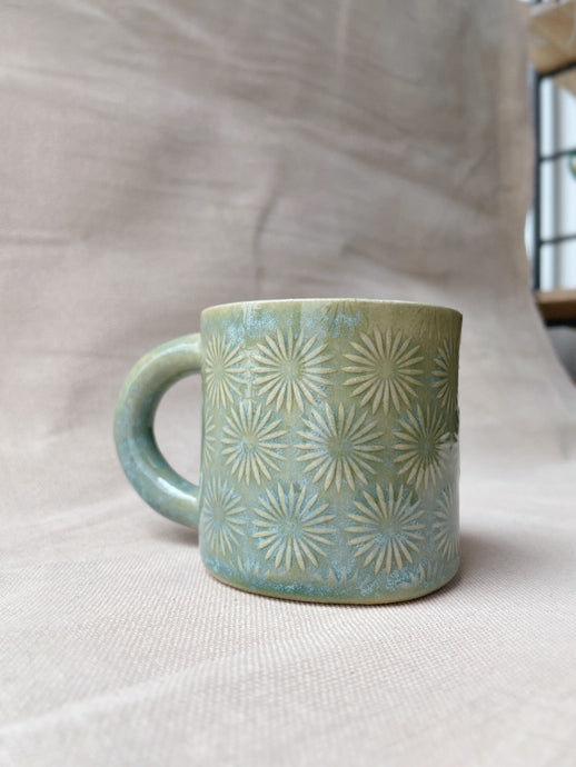 taza de cerámica hecha a mano con esmalte verde brillante y chipas turquesas y relieve de margaritas.
