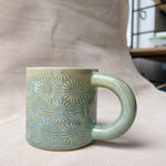 taza de cerámica hecha a mano con esmalte verde brillante y chipas turquesas y relieve de margaritas.