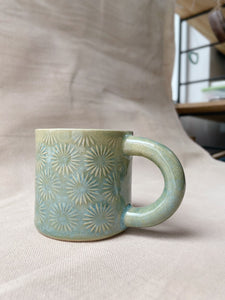 taza de cerámica hecha a mano con esmalte verde brillante y chipas turquesas y relieve de margaritas.